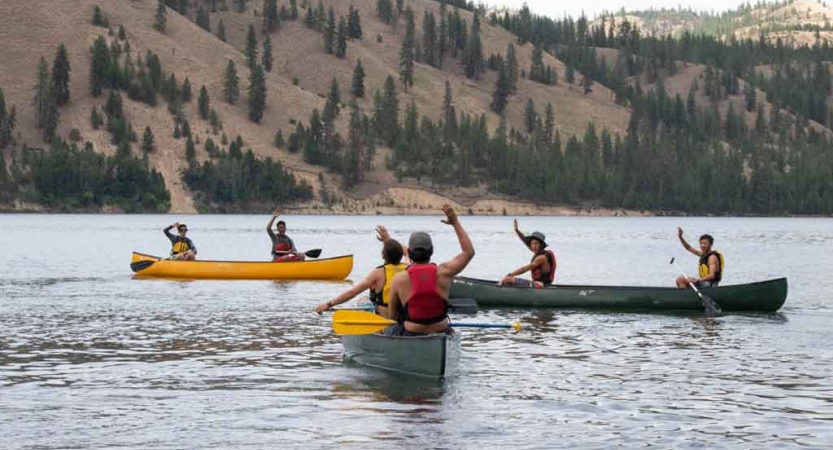 a group of boys in canoes wave at the camera on an outward bound trip